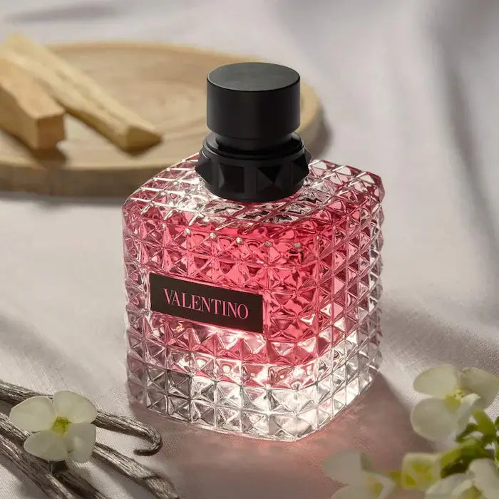 VALENTINO DONNA BORN IN ROMA EAU DE PARFUM WITH BOURBON VANILLA & JASMINE bottle on a table with flowers.